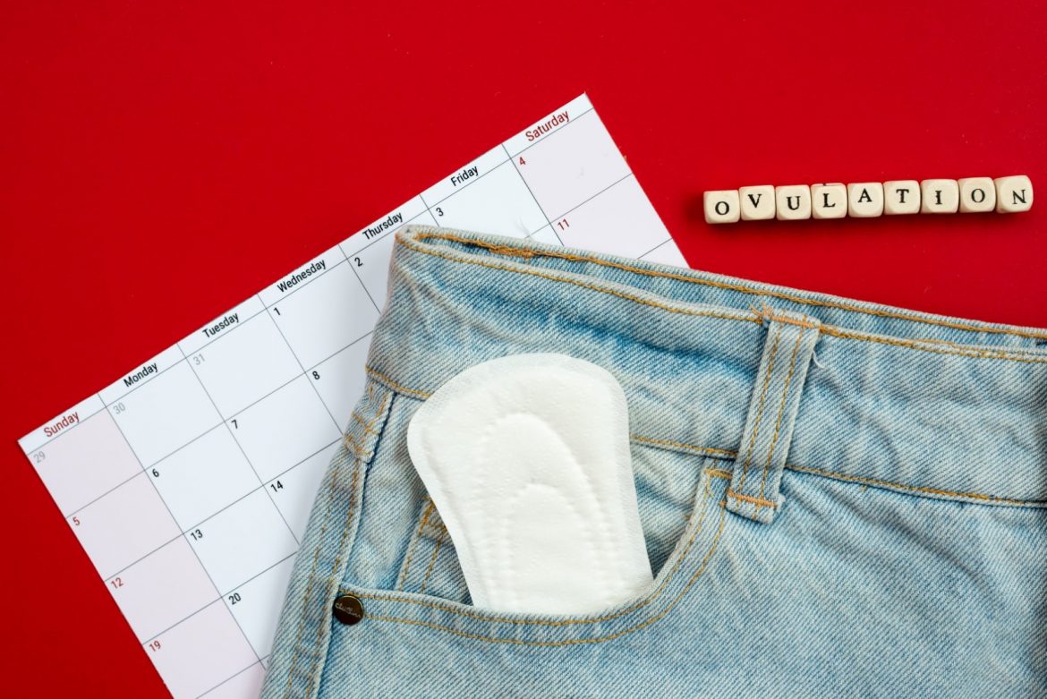 Tracking the menstrual cycle and ovulation. on a red background women’s pads in jeans pocket. Zaburzenia cyklu miesiączkowego – czy stres może być główną przyczyną?